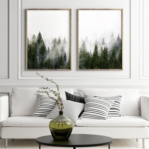 May include: Two framed prints of a misty forest with tall evergreen trees. The prints are hanging on a white wall above a white couch with black and white striped throw pillows.