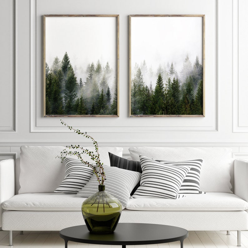 May include: Two framed prints of a misty forest with tall evergreen trees. The prints are hanging on a white wall above a white couch with black and white striped throw pillows.