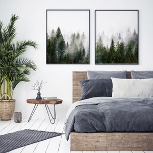 May include: A bedroom with a wooden bed frame and a gray duvet. Two framed prints of a foggy forest scene hang above the bed. A small wooden side table with a metal base sits next to the bed.