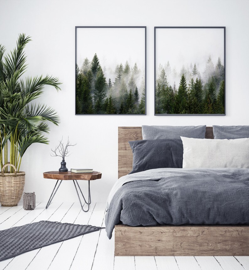 May include: A bedroom with a wooden bed frame and a gray duvet. Two framed prints of a foggy forest scene hang above the bed. A small wooden side table with a metal base sits next to the bed.