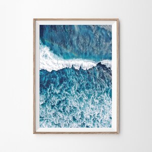 May include: An aerial photograph of a blue ocean with white foamy waves crashing. The water is a deep blue color and the waves are white and foamy. The photo was taken from a high angle, giving a unique perspective of the ocean.