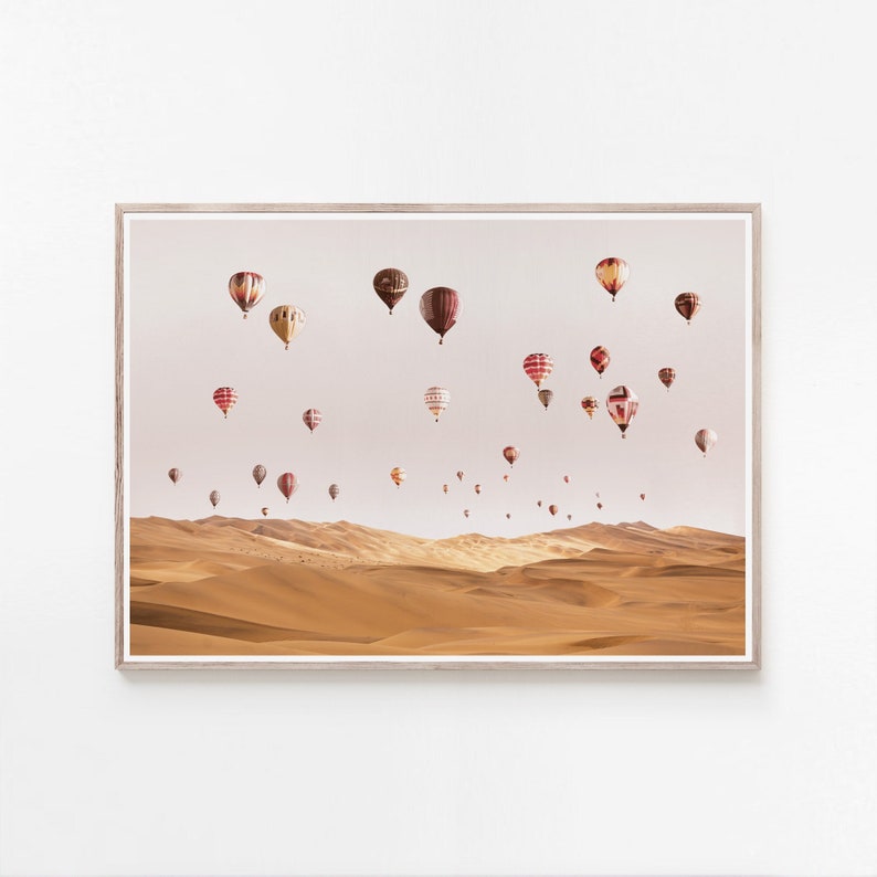 May include: A framed photograph of a desert landscape with a large number of hot air balloons in the sky. The balloons are various shades of red, white, and brown, and they are flying over a vast expanse of sand dunes.