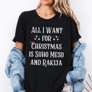 May include: Black t-shirt with white text that reads "All I want for Christmas is Suho Meso and Rakija".