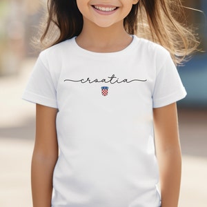 May include: White t-shirt with the word "croatia" written in cursive and the Croatian coat of arms in the center.