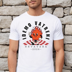 May include: White t-shirt featuring a cartoon flame character with the text "IDEMO VATRENI" and "HRVATSKA - 2026". The flame character is red with black accents, standing on a red and white checkered pattern.