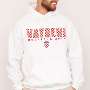 May include: White hoodie with a front pocket and drawstring. The front features the word "VATRENI" in red checkered letters, "HRVATSKA 2026" in red, and a Croatian coat of arms.