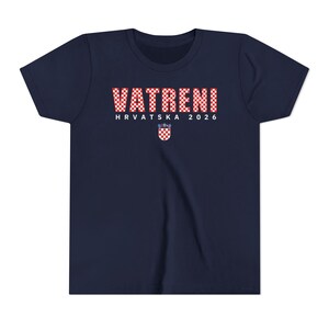 May include: Navy blue t-shirt with the text "VATRENI HRVATSKA 2026" in red and white checkered letters. A Croatian coat of arms is below the text. The shirt is a youth size.