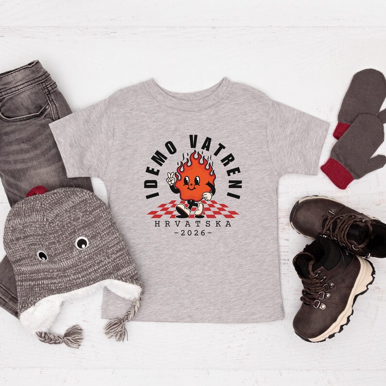 May include: A light gray toddler t-shirt with a cartoon flame character and the text "IDEMO VATRENI HRVATSKA -2026-". The shirt is surrounded by a gray beanie, gray jeans, brown boots, and gray mittens.