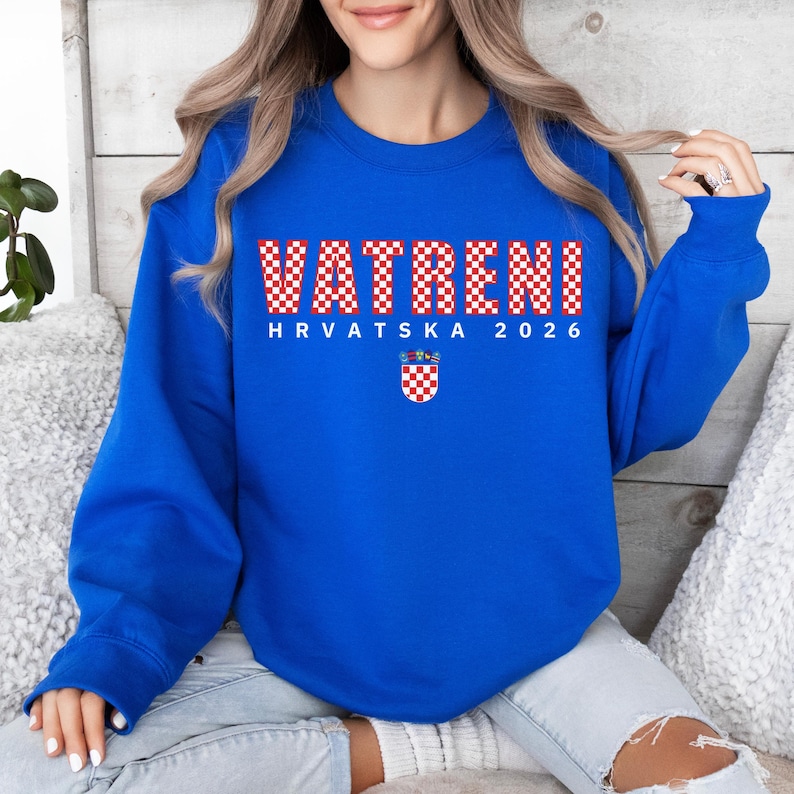 May include: A royal blue sweatshirt featuring the word "VATRENI" in a red and white chequered pattern. Below is "HRVATSKA 2026" and a Croatian coat of arms. The sweatshirt has long sleeves and is a casual garment.
