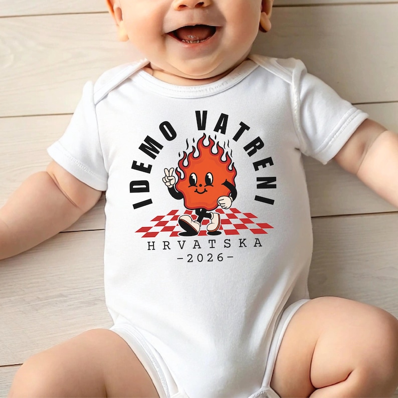 Puede incluir: Body de beb&eacute; blanco con un personaje de llama de dibujos animados. La llama es naranja con una cara sonriente, haciendo el signo de la paz. El texto en el body dice "IDEMO VATRENI" y "HRVATSKA -2026-" en negro.