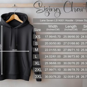 May include: A black hoodie displayed on a wooden hanger, with a sizing chart to the right. The chart provides measurements for width, length, and sleeve length in inches and centimeters for sizes XS to 3XL. The hoodie has a front pocket and a drawstring hood.