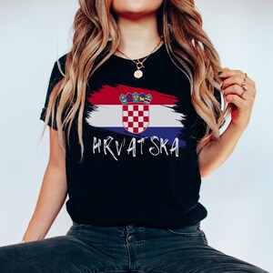 May include: Black t-shirt featuring a white paint-splattered Croatian flag and the word "HRVATSKA" in white lettering.
