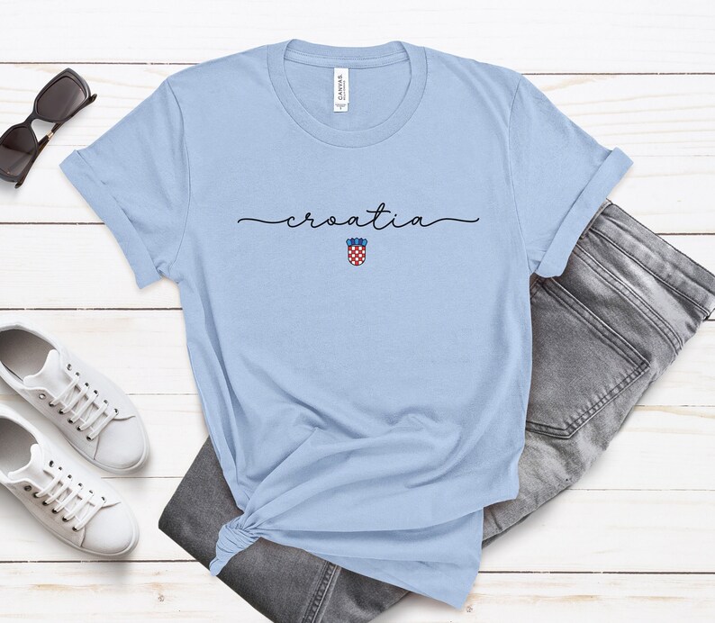 May include: Light blue t-shirt with the word "croatia" written in cursive and a small Croatian coat of arms graphic.