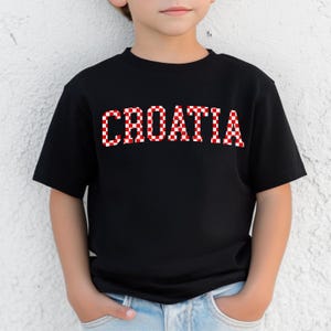 May include: Black t-shirt with the word "CROATIA" in red and white checkered letters. The shirt is short-sleeved and appears to be made of cotton. The design is centered on the chest.