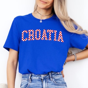 May include: A royal blue t-shirt with the word "CROATIA" printed across the chest in a red and white checkered pattern. The shirt is short-sleeved and made of a soft material.