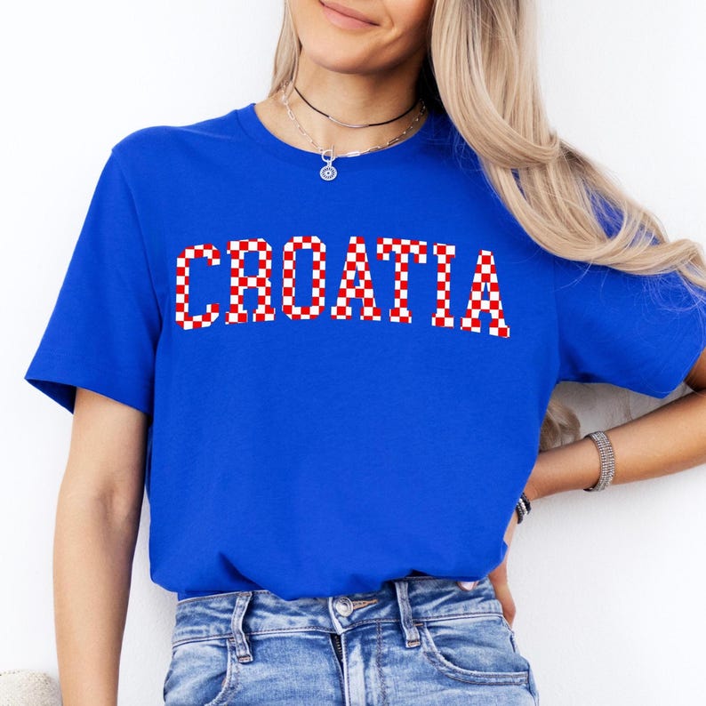 May include: A royal blue t-shirt with the word "CROATIA" printed across the chest in a red and white checkered pattern. The shirt is short-sleeved and made of a soft material.