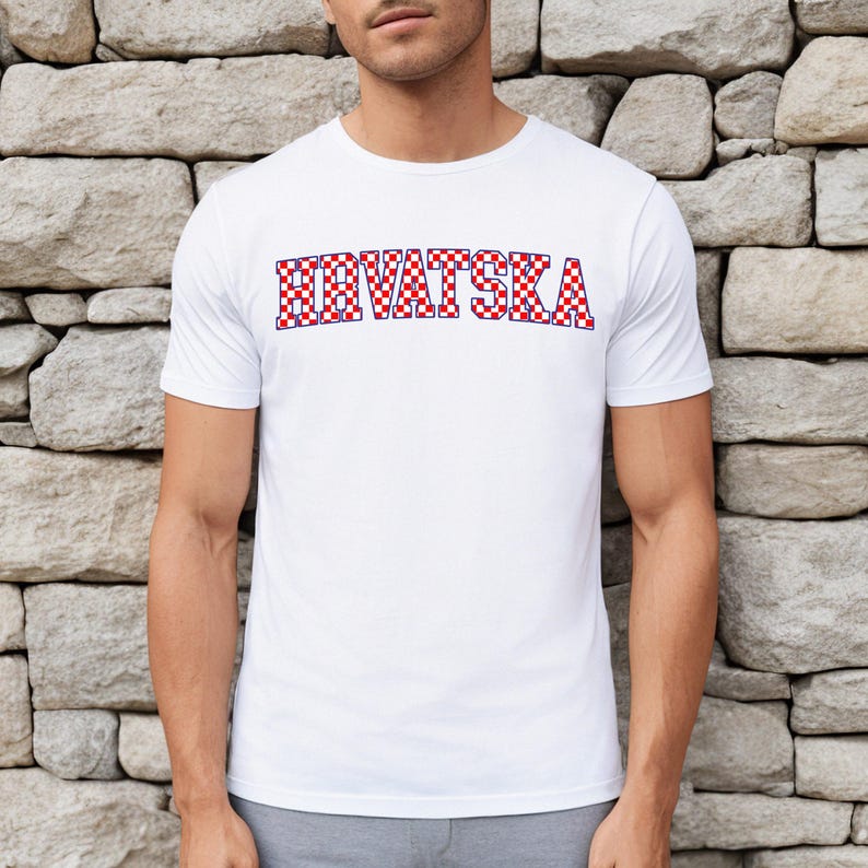 May include: White t-shirt featuring the word "HRVATSKA" in a red and blue chequered design. The shirt has short sleeves and a crew neck. The text is in a bold, blocky font.