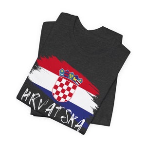 May include: A dark grey t-shirt with a white paint-splattered Croatian flag and the word "HRVATSKA" in white lettering.