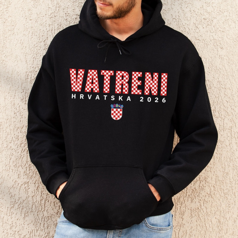 May include: Black hooded sweatshirt with the word "VATRENI" in red and white checkered letters. Below the word is "HRVATSKA 2026" in white text, with a Croatian coat of arms. The sweatshirt has a front pocket and a drawstring hood.