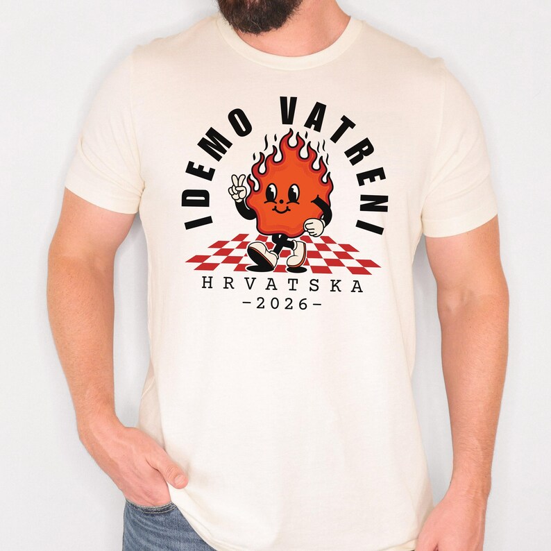 May include: Cream-colored t-shirt featuring a cartoon flame character with a peace sign, set against a red and white checkered background. The shirt has the text "IDEMO VATRENI" and "HRVATSKA - 2026-" in black.