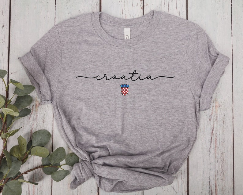May include: Gray t-shirt with the word "croatia" written in cursive script and a small Croatian coat of arms below it.