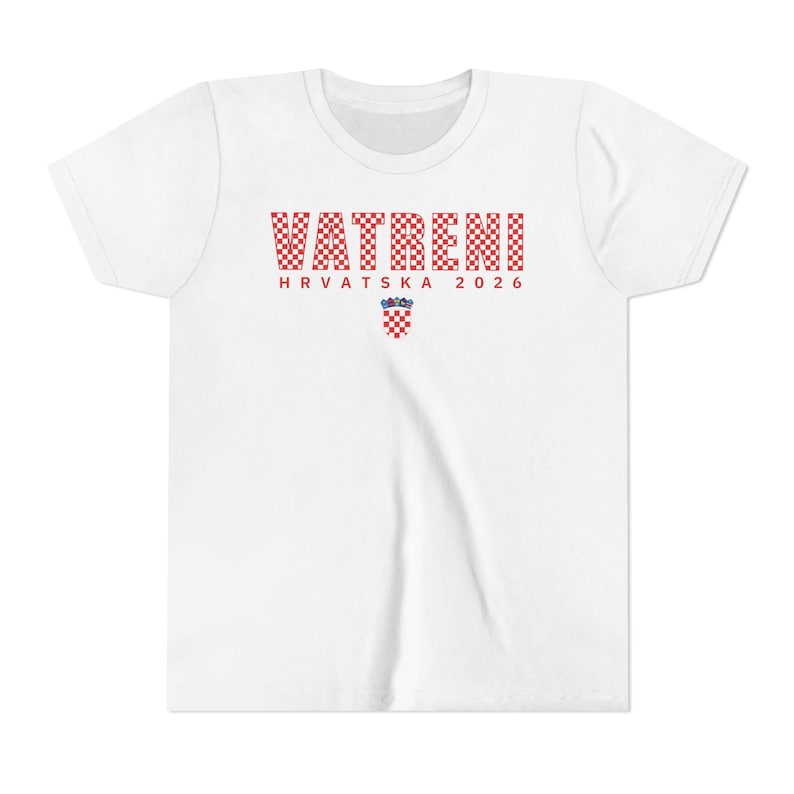 May include: White t-shirt with the word "VATRENI" in red and white checkered letters. Below the word is "HRVATSKA 2026" in red letters, and a Croatian coat of arms. The shirt has short sleeves and a crew neck.