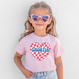 May include: A pink t-shirt with a red and white checkered heart that says "CROATIA" in blue letters.