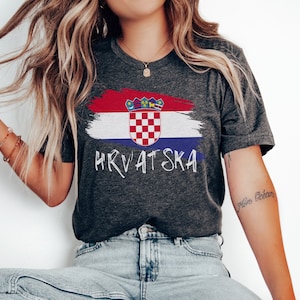 May include: A dark grey t-shirt featuring a white paint-splattered Croatian flag design and the word "HRVATSKA" in white lettering.