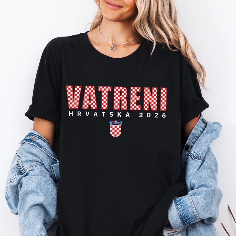 May include: Black t-shirt with the word "VATRENI" in red and white checkered letters. Below the word is "HRVATSKA 2026" in white letters, and a Croatian coat of arms. The shirt is a casual style.