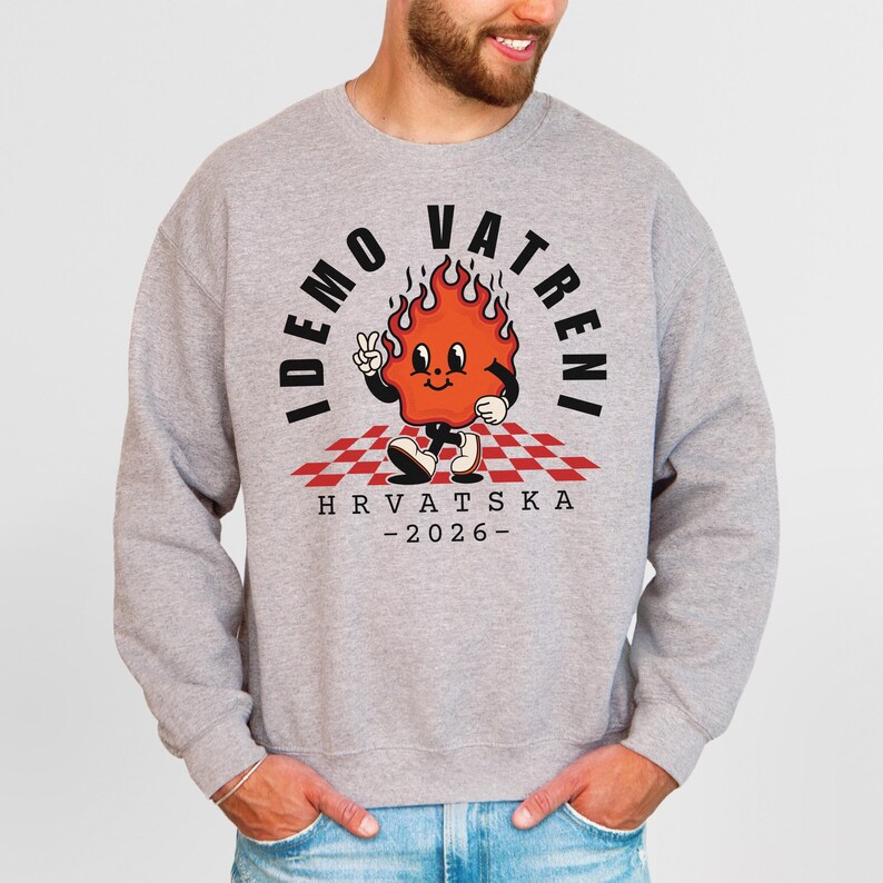 May include: A light gray sweatshirt featuring a cartoon flame character with the text "IDEMO VATRENI" and "HRVATSKA - 2026". The flame character is orange with black accents, standing on a red and white checkered pattern.