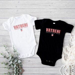 K&ouml;nnte beinhalten: Zwei Baby-Bodys, einer wei&szlig; und einer schwarz, werden auf einer hellen Holzoberfl&auml;che gezeigt. Jeder Body hat das Wort "VATRENI" in rot karierten Buchstaben, darunter "HRVATSKA 2026" und ein kroatisches Wappen.