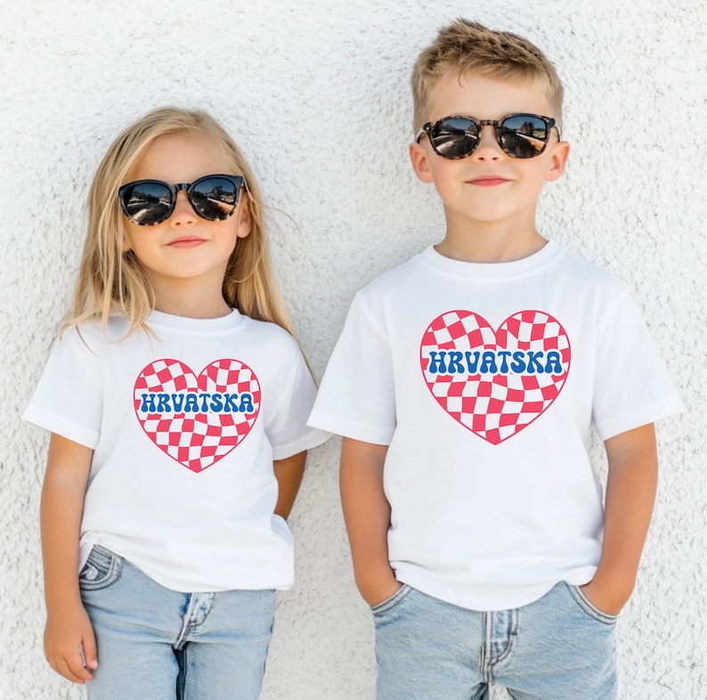 Puede incluir: Dos ni&ntilde;os con camisetas blancas con un dise&ntilde;o de coraz&oacute;n a cuadros rojo y blanco y la palabra "HRVATSKA" en letras azules. Los ni&ntilde;os llevan gafas de sol y sonr&iacute;en.