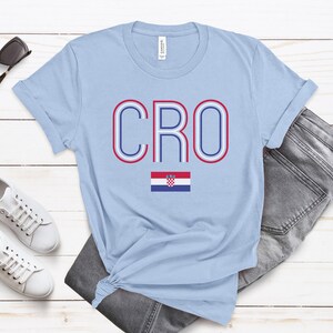 May include: Light blue t-shirt with the word "CRO" in red, white, and blue outlined letters. The Croatian flag is below the word.