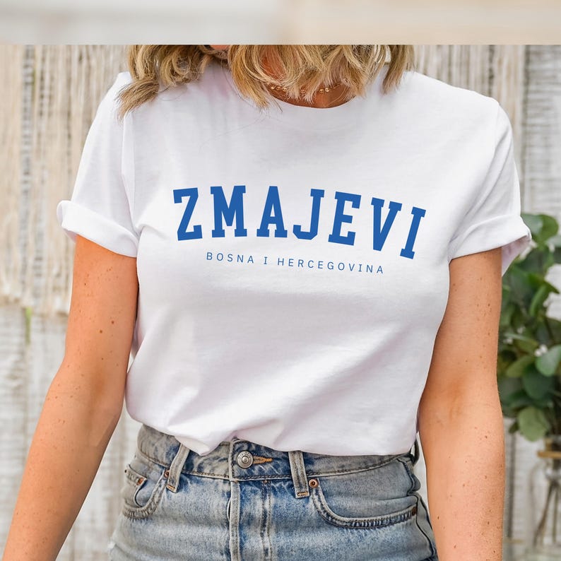 Op de afbeelding: Wit T-shirt met blauwe tekst die "ZMAJEVI" en "BOSNA I HERCEGOVINA" zegt.