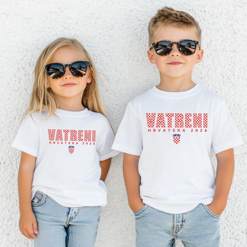 May include: Two children wearing white t-shirts with the word "VATRENI" in red checkered letters. Below the word is "HRVATSKA 2026" in red letters and a Croatian coat of arms. Both children are wearing sunglasses.