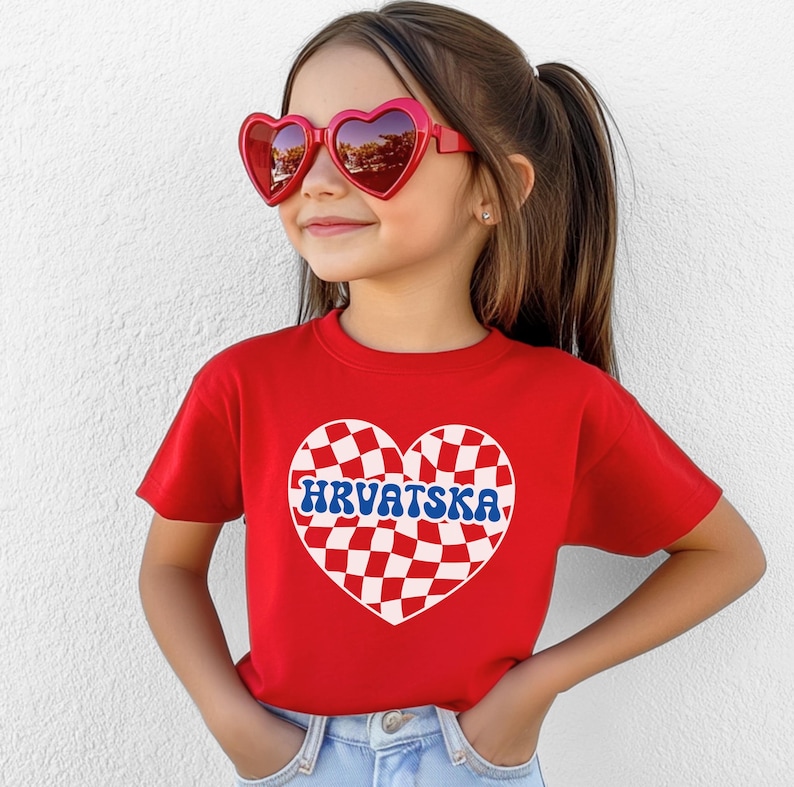 Puede incluir: Camiseta roja con un dise&ntilde;o de coraz&oacute;n a cuadros y la palabra "HRVATSKA" en letras azules. La camiseta la lleva puesta una ni&ntilde;a con gafas de sol rojas en forma de coraz&oacute;n.