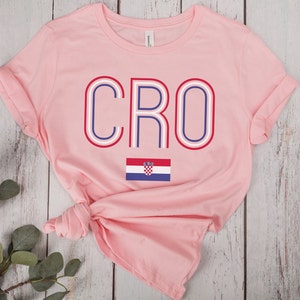 May include: Pink t-shirt with the word "CRO" in red, white, and blue with a stylized outline. The Croatian flag is below the word.