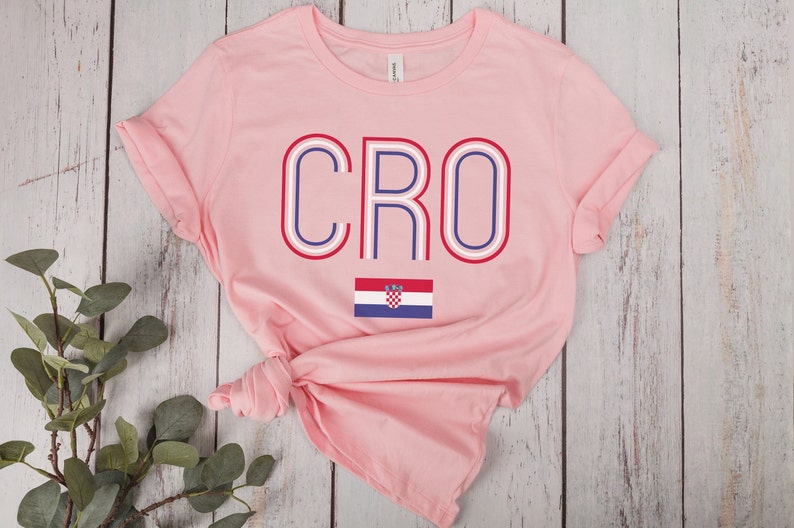 May include: Pink t-shirt with the word "CRO" in red, white, and blue with a stylized outline. The Croatian flag is below the word.