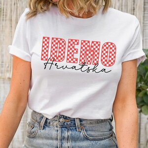 May include: White t-shirt with a red and white checkered design that spells out "IDEMO" and the text "Hrvatska" in black script.