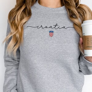 May include: Gray sweatshirt with the word "croatia" written in cursive and the Croatian coat of arms in red, white, and blue.