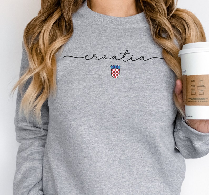 May include: Gray sweatshirt with the word "croatia" written in cursive and the Croatian coat of arms in red, white, and blue.