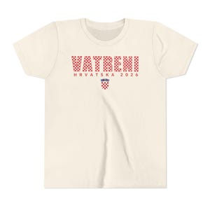 May include: Cream-colored t-shirt with the word "VATRENI" in red and white checkered letters. Below, the text "HRVATSKA 2026" is printed in red. A Croatian coat of arms is centered below the text.