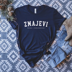 Op de afbeelding: Een marineblauw t-shirt met witte tekst die "ZMAJEVI" en "BOSNA I HERCEGOVINA" zegt.