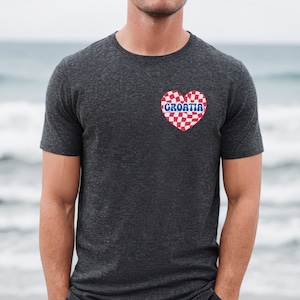 Puede incluir: Una camiseta gris oscuro con un coraz&oacute;n a cuadros rojo y blanco con la palabra "CROATIA" en letras azules.