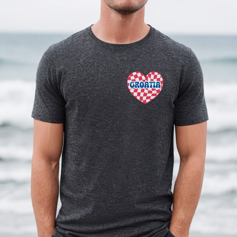 Puede incluir: Una camiseta gris oscuro con un coraz&oacute;n a cuadros rojo y blanco con la palabra "CROATIA" en letras azules.