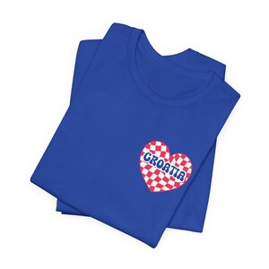 Puede incluir: Una camiseta azul real con un coraz&oacute;n a cuadros rojo y blanco con la palabra "CROATIA" escrita en una fuente retro.