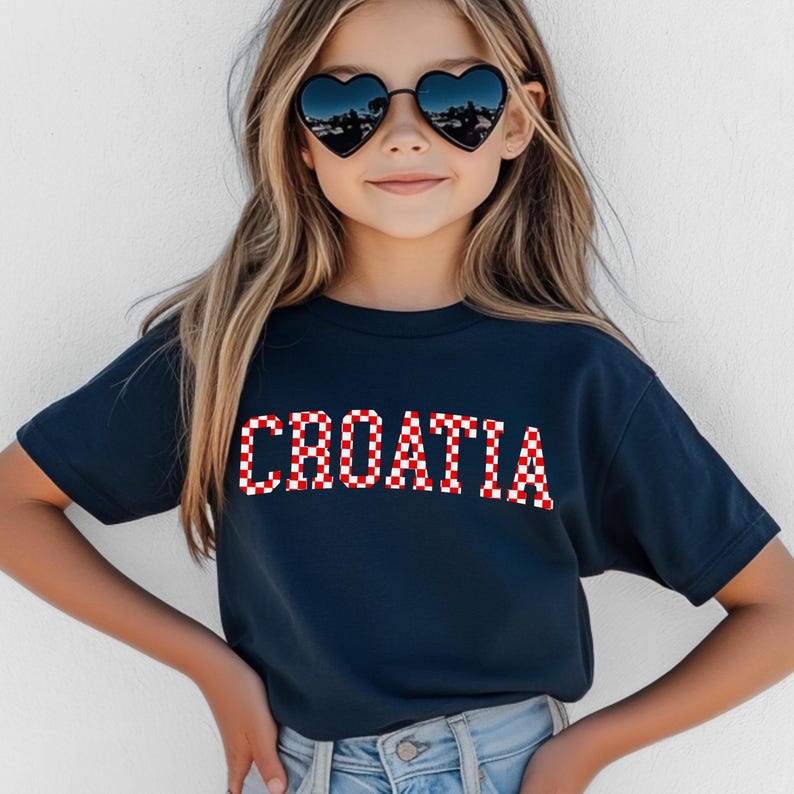 May include: A navy blue t-shirt with the word "CROATIA" in red and white checkered letters. The shirt is short-sleeved and worn by a person wearing heart-shaped sunglasses.