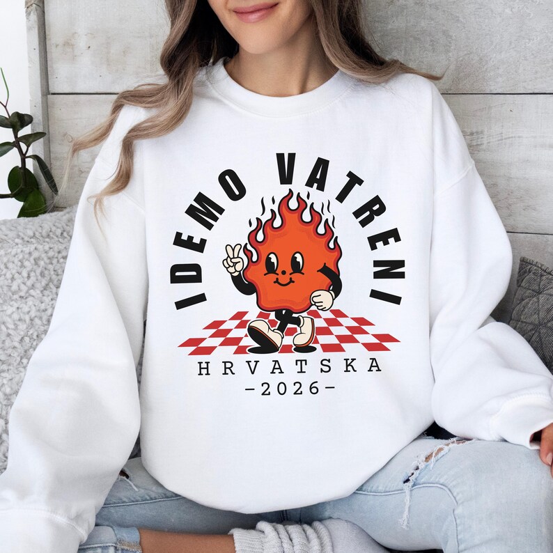 May include: White sweatshirt with a cartoon flame character giving a peace sign. The design includes the text "IDEMO VATRENI" and "HRVATSKA - 2026-" in black. The flame character is on a red and white checkered pattern.