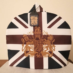 May include: A white, brown, and black teapot cover with a Union Jack design. The cover features a gold royal coat of arms with the text "DIEU ET MON DROIT". The tag on the cover reads "AGM Gifts & More" and "Made in USA".