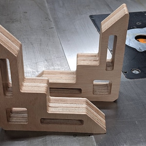 May include: Two wooden corner brackets made of layered plywood with cut-out designs. The brackets are stacked on top of each other.